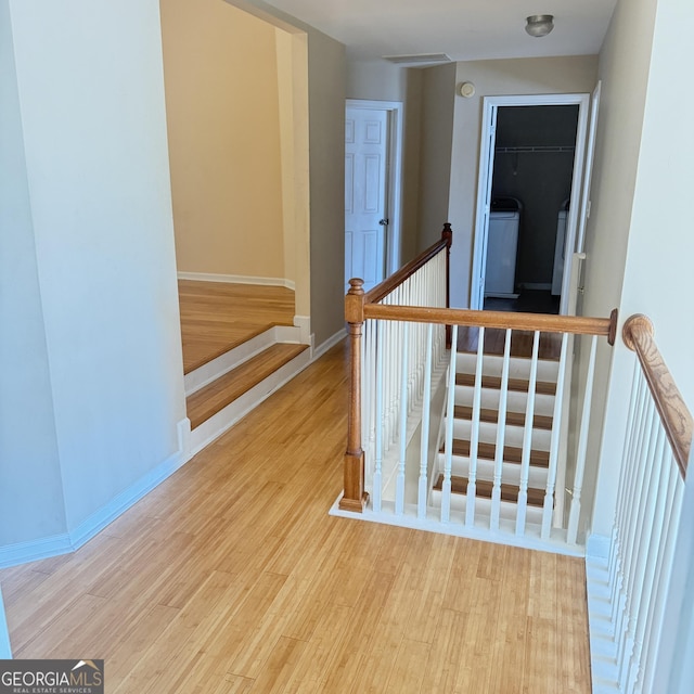 hallway with washer / clothes dryer, visible vents, wood finished floors, an upstairs landing, and baseboards