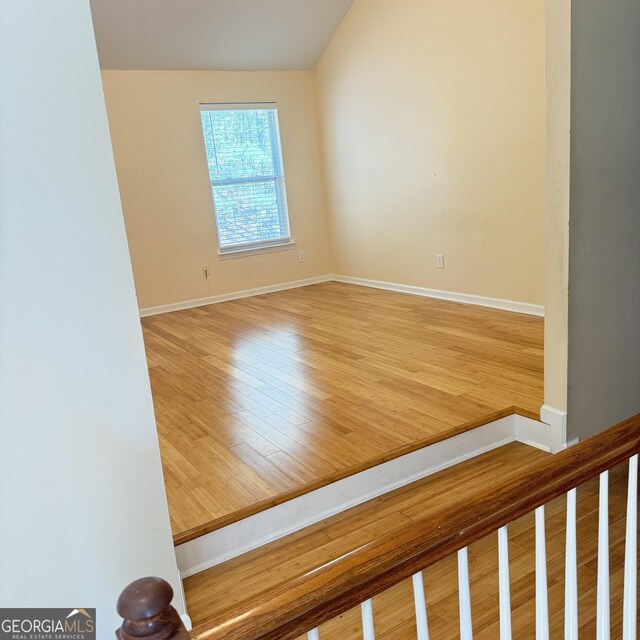 empty room featuring baseboards, vaulted ceiling, and wood finished floors