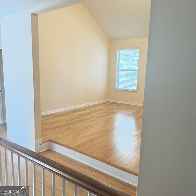 interior space featuring wood finished floors, baseboards, and vaulted ceiling