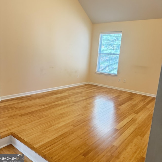 spare room featuring light wood-type flooring, baseboards, and lofted ceiling