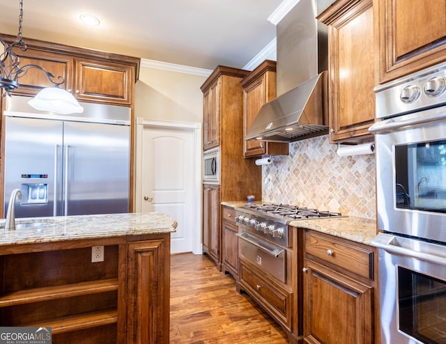 kitchen featuring brown cabinetry, crown molding, wall chimney exhaust hood, and built in appliances