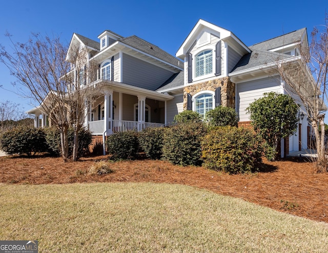 view of front of home featuring a garage, stone siding, a porch, and a front yard