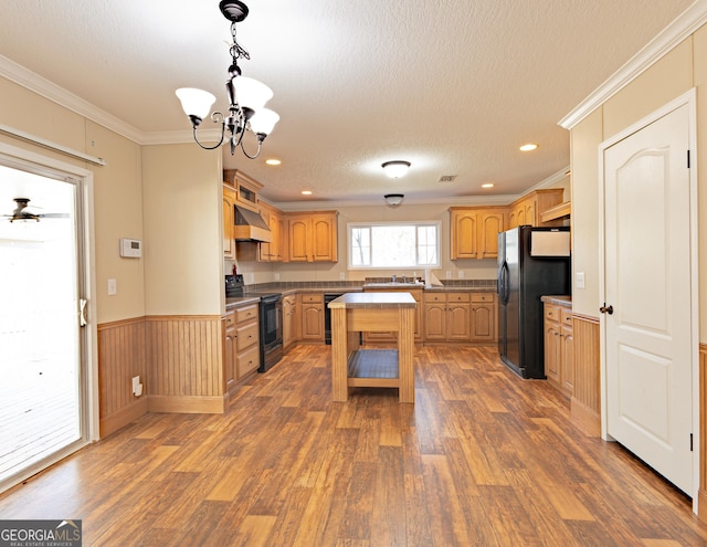 kitchen featuring wood finished floors, exhaust hood, wainscoting, black appliances, and crown molding