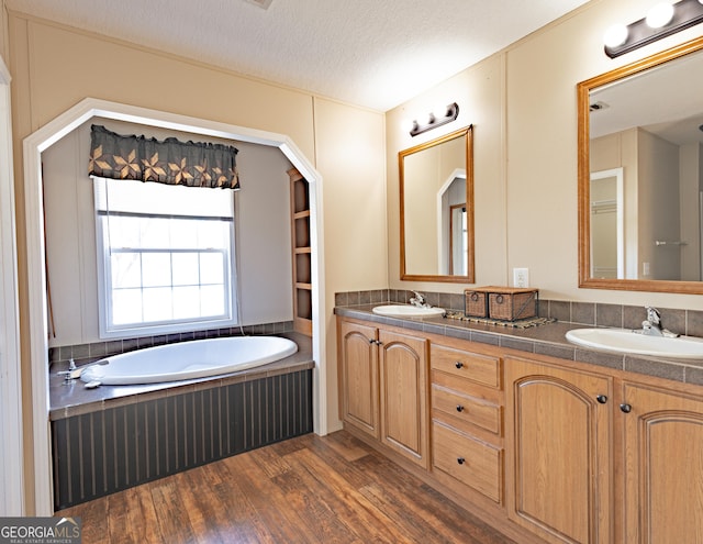 full bath featuring double vanity, wood finished floors, a sink, a textured ceiling, and a bath