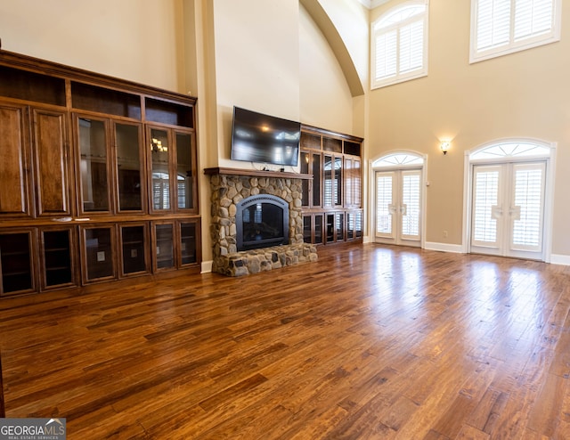 unfurnished living room featuring french doors, plenty of natural light, a stone fireplace, and wood finished floors