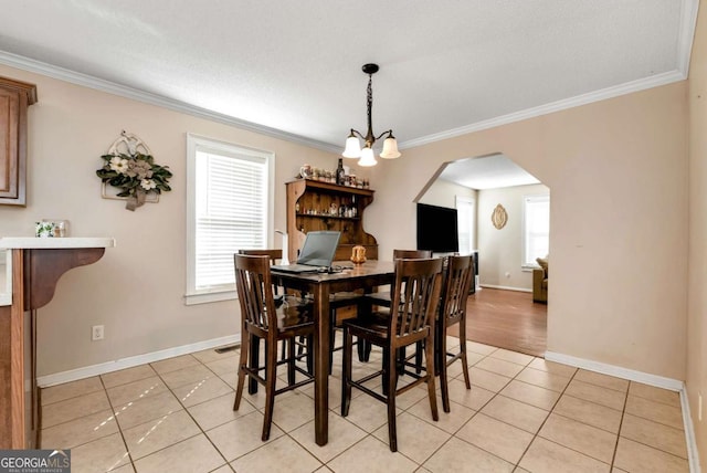 dining room featuring arched walkways, ornamental molding, light tile patterned flooring, and baseboards