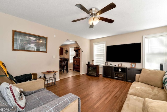 living area with arched walkways, a textured ceiling, wood finished floors, and a healthy amount of sunlight