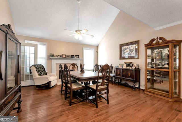 dining space featuring a healthy amount of sunlight, vaulted ceiling, a tiled fireplace, and wood finished floors