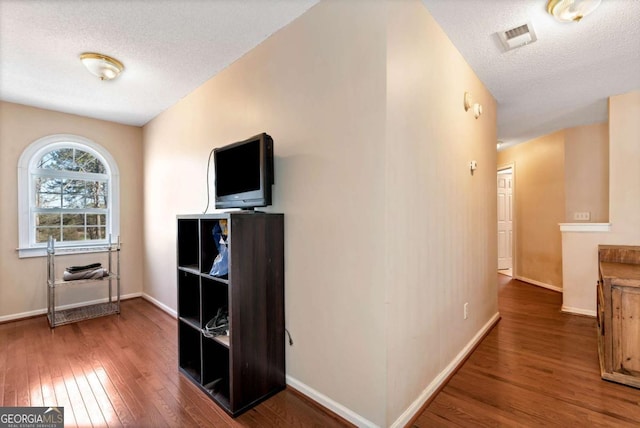 hallway featuring hardwood / wood-style flooring, baseboards, visible vents, and a textured ceiling