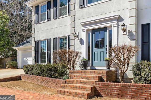 view of exterior entry with driveway, an attached garage, and stucco siding