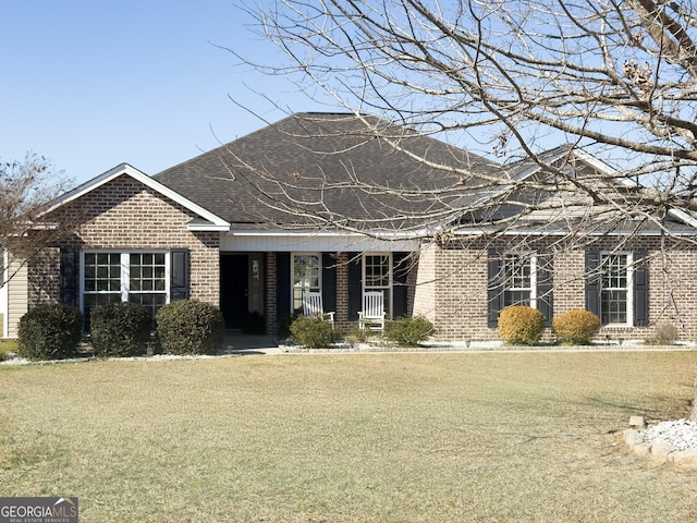 view of front of property featuring a front yard, brick siding, and roof with shingles