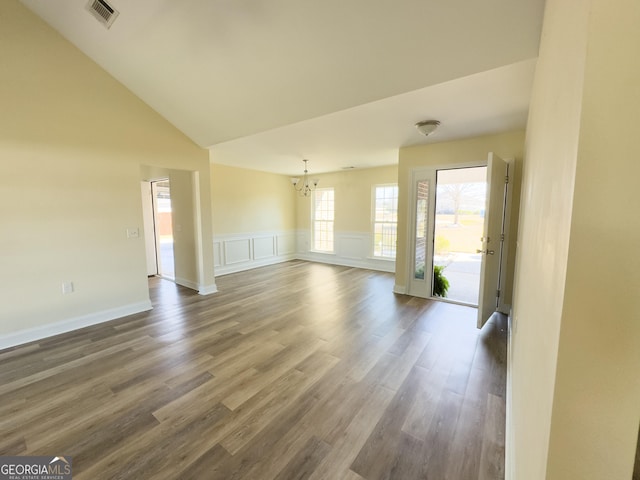 unfurnished living room featuring dark wood-style flooring, a wainscoted wall, a notable chandelier, visible vents, and a decorative wall