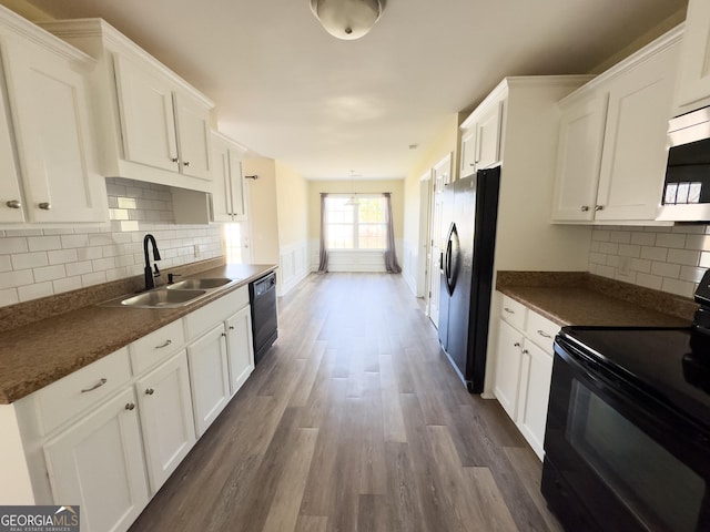 kitchen featuring dark countertops, black appliances, white cabinets, and a sink