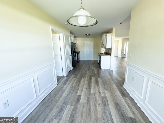 corridor with a wainscoted wall, a sink, a decorative wall, and wood finished floors