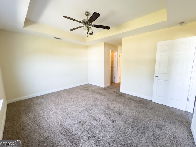 unfurnished bedroom featuring visible vents, baseboards, ceiling fan, carpet, and a tray ceiling