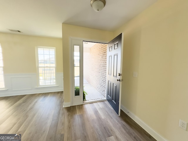 foyer entrance featuring a wainscoted wall, a decorative wall, visible vents, and wood finished floors