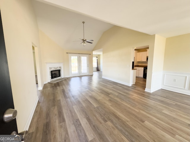 unfurnished living room with a ceiling fan, a wainscoted wall, wood finished floors, french doors, and a high end fireplace