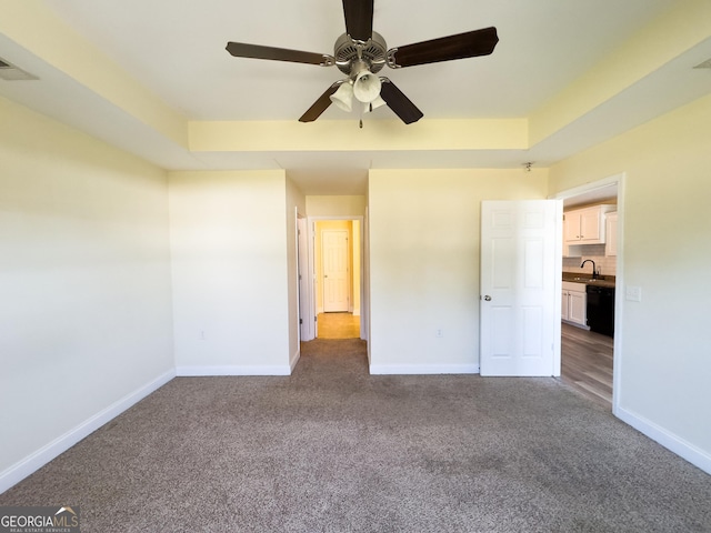 unfurnished bedroom featuring carpet floors, a tray ceiling, a sink, and baseboards