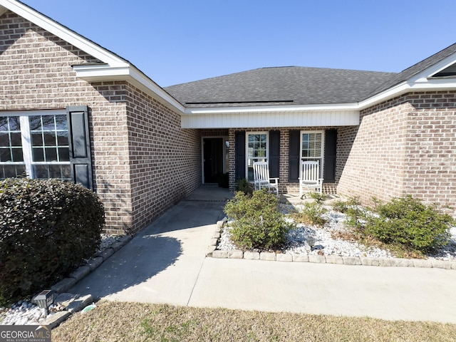 property entrance featuring brick siding, a porch, and roof with shingles