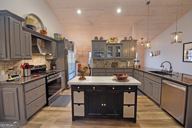 kitchen featuring stainless steel appliances, vaulted ceiling, a sink, a peninsula, and wall chimney exhaust hood