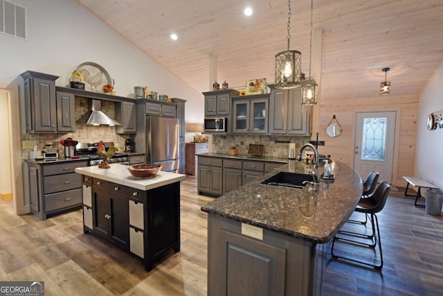 kitchen featuring stainless steel appliances, a kitchen island, a sink, visible vents, and wall chimney range hood