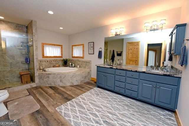 bathroom featuring double vanity, a stall shower, wood finished floors, a garden tub, and a sink