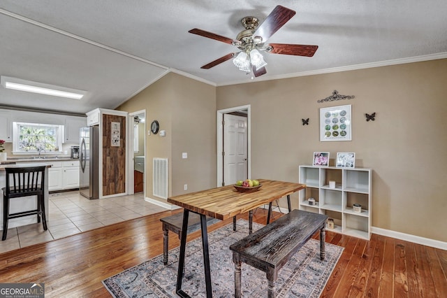 dining area featuring light wood finished floors, baseboards, visible vents, a ceiling fan, and ornamental molding