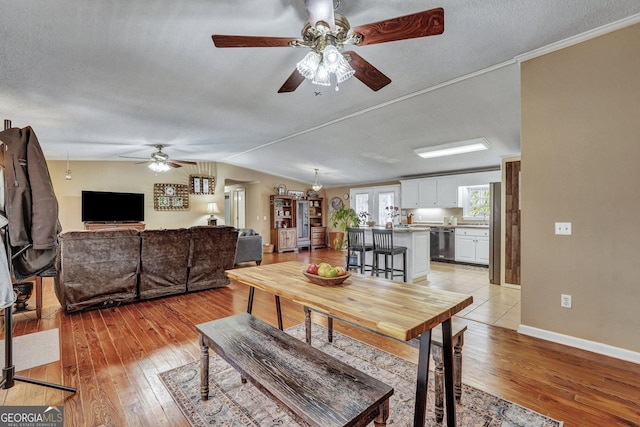 dining area featuring lofted ceiling, baseboards, light wood-style flooring, and a textured ceiling