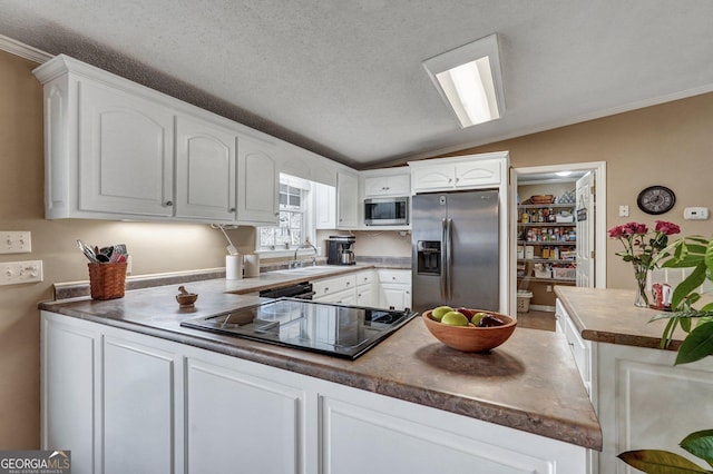 kitchen featuring white cabinets, a peninsula, vaulted ceiling, stainless steel appliances, and a sink