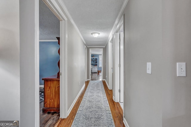 hallway featuring crown molding, a textured ceiling, baseboards, and wood finished floors