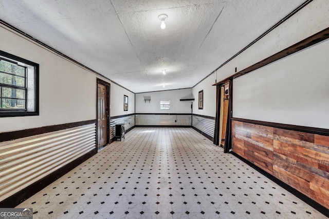 corridor with ornamental molding, a wainscoted wall, plenty of natural light, and a textured ceiling