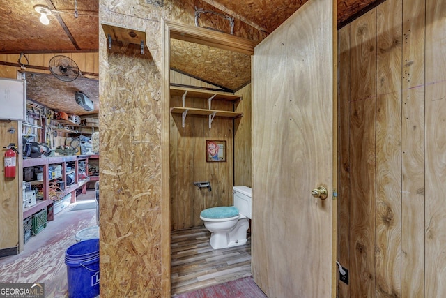 bathroom featuring toilet, wooden walls, vaulted ceiling, and wood finished floors