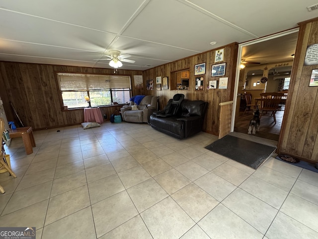 unfurnished living room with wood walls, ceiling fan, visible vents, and light tile patterned flooring