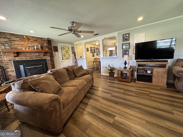 living room featuring crown molding, decorative columns, a brick fireplace, a textured ceiling, and wood finished floors