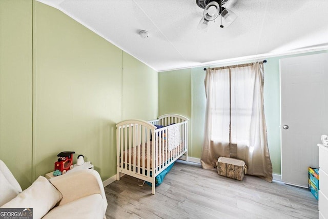 bedroom featuring vaulted ceiling, a textured ceiling, wood finished floors, a crib, and baseboards