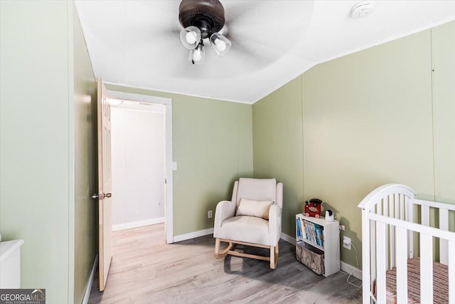 bedroom with baseboards, a ceiling fan, lofted ceiling, wood finished floors, and a nursery area