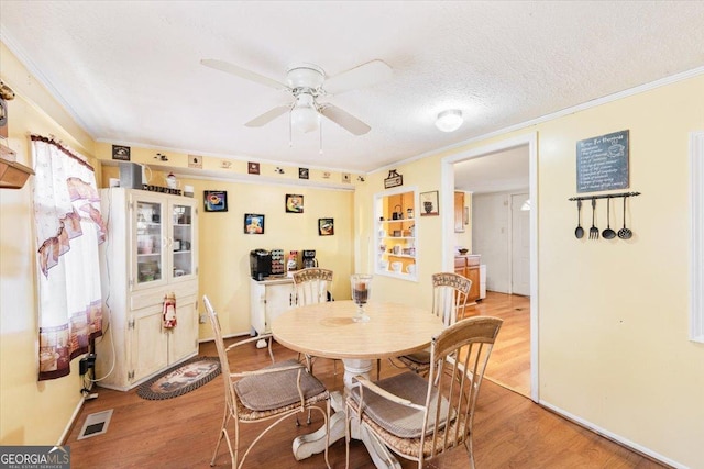 dining area with light wood-style floors, crown molding, visible vents, and a textured ceiling