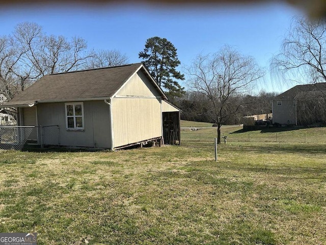 view of side of home with an outbuilding, roof with shingles, a lawn, and fence