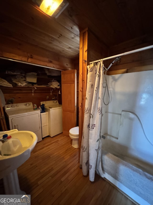 full bathroom featuring a shower with curtain, toilet, wooden walls, wood finished floors, and washer and dryer