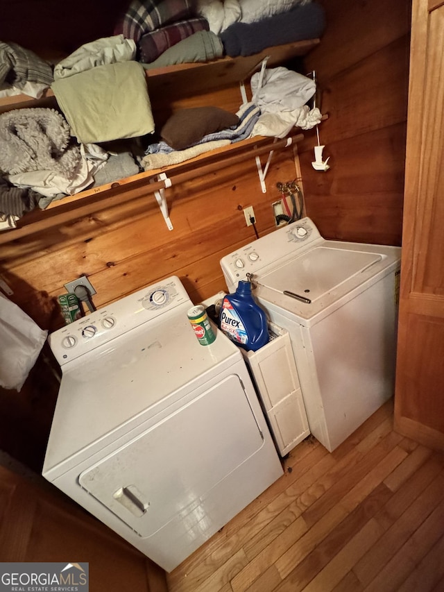 laundry room with wooden walls, wood finished floors, and washer and dryer