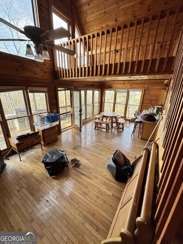 living room with high vaulted ceiling, ceiling fan, wooden walls, and hardwood / wood-style flooring