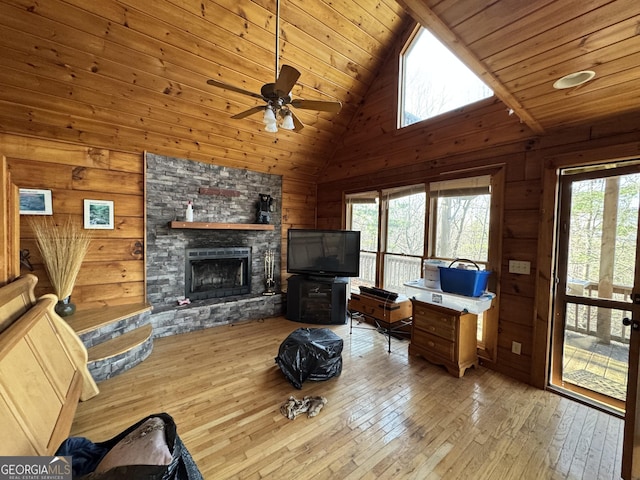 living area with ceiling fan, a stone fireplace, wooden walls, wood ceiling, and hardwood / wood-style floors