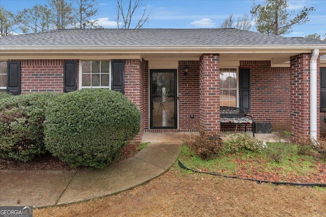 doorway to property featuring brick siding and a shingled roof