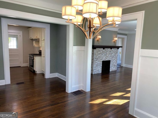 unfurnished dining area with visible vents, dark wood finished floors, an inviting chandelier, crown molding, and a fireplace