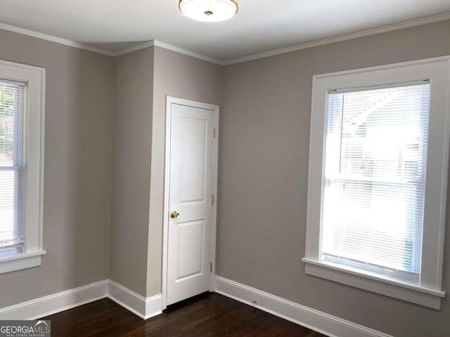 empty room featuring dark wood-style floors, plenty of natural light, baseboards, and ornamental molding