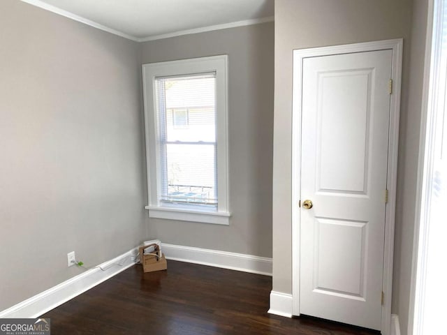 empty room with ornamental molding, dark wood-style flooring, and baseboards