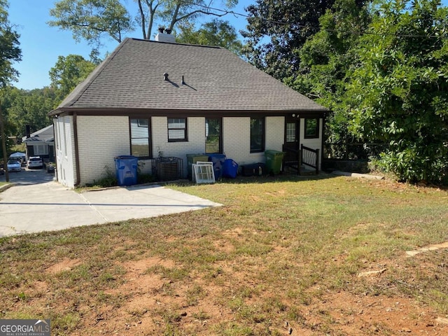 back of property with brick siding, driveway, roof with shingles, a lawn, and a chimney