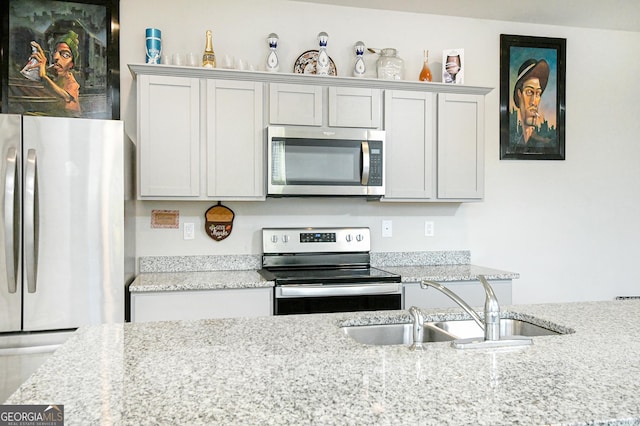 kitchen featuring light stone countertops, stainless steel appliances, and a sink