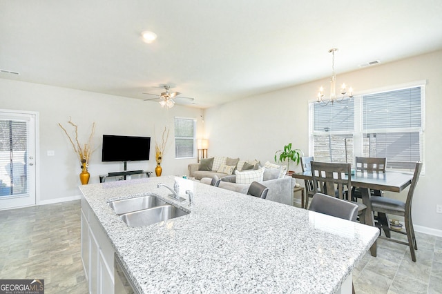 kitchen featuring a center island with sink, baseboards, visible vents, a sink, and ceiling fan with notable chandelier