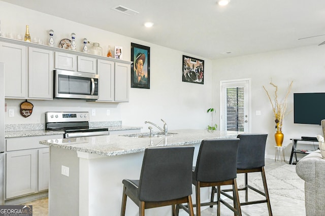 kitchen featuring a center island with sink, visible vents, light stone countertops, stainless steel appliances, and a sink